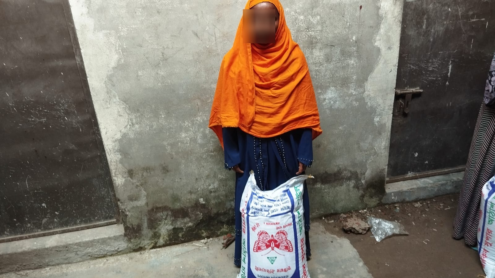 Woman in an orange headscarf with a sack of rice from the distribution