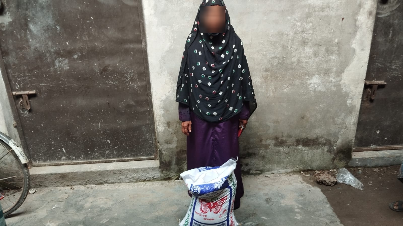 Woman in a black headscarf standing behind a sack of rice