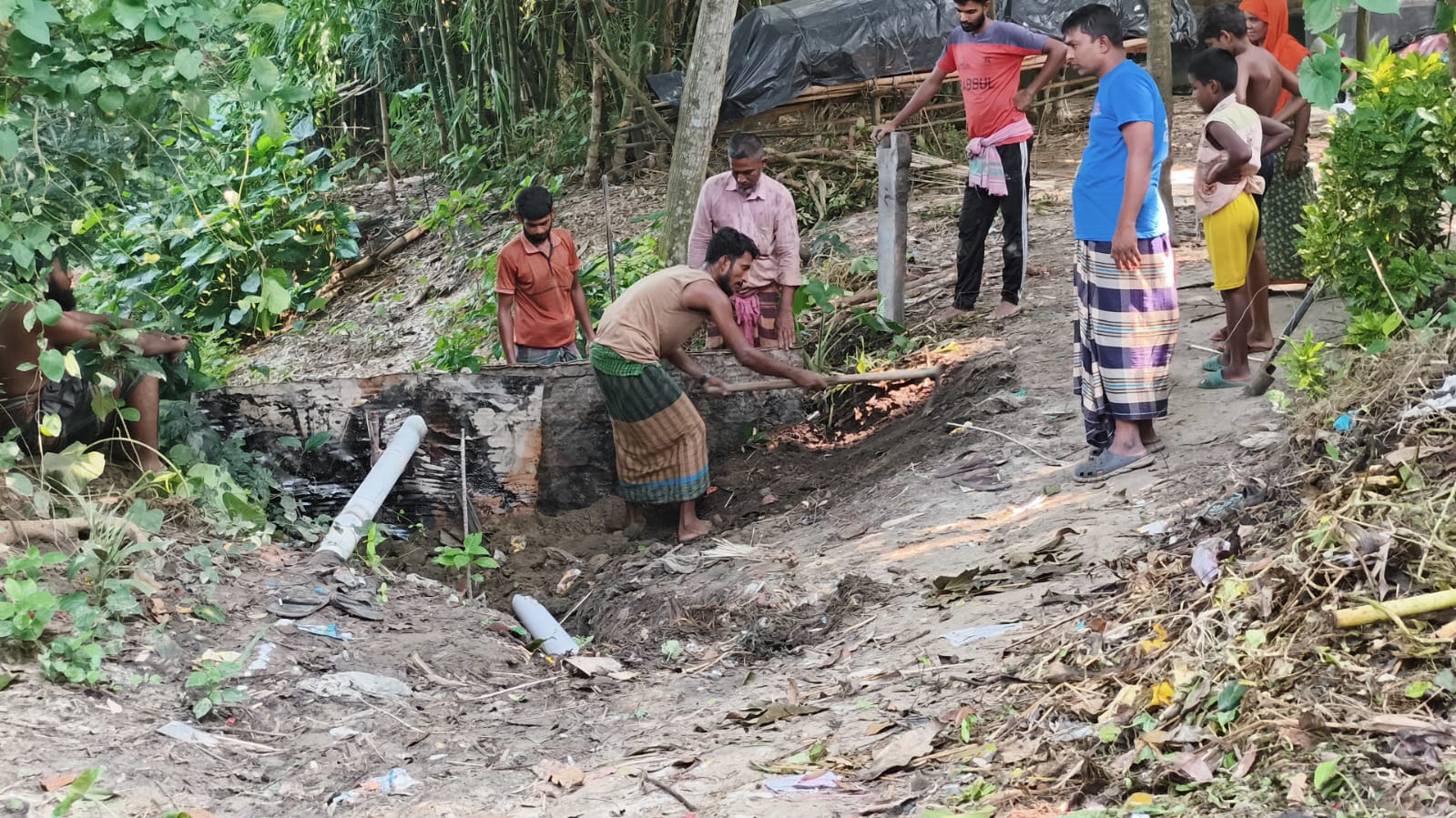 Villagers digging beside a drain pipe to repair the village path