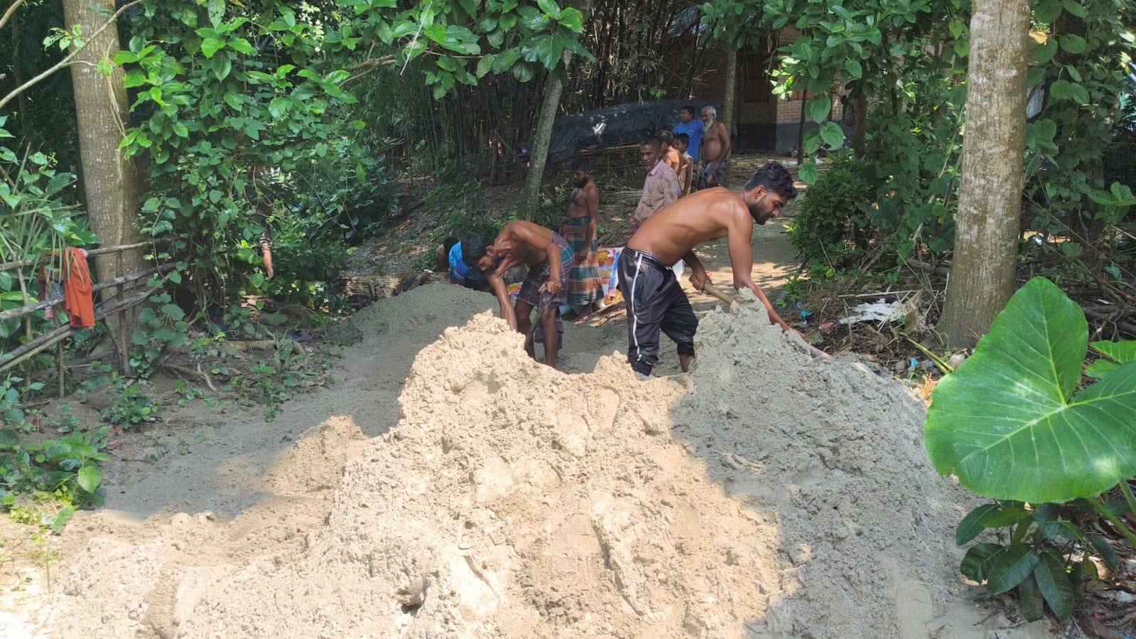Volunteers shovelling sand to raise the village path